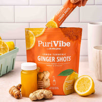 PuriVibe Lemon Turmeric Ginger Shots packaging with a hand holding a shot stick, lemons, and ginger on a countertop.