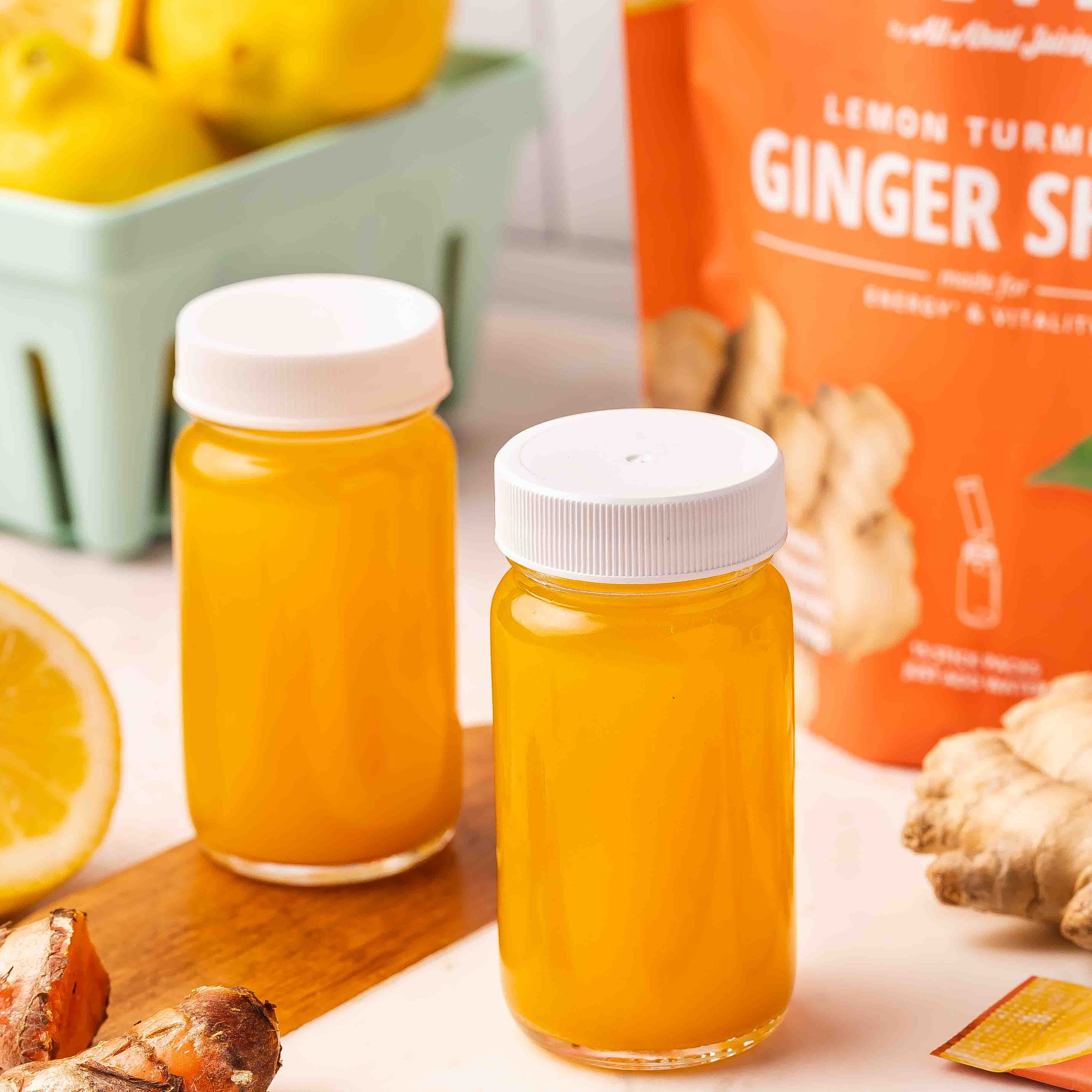 Two bottles of ginger turmeric juice with a box of PuriVibe Ginger bag on a table.