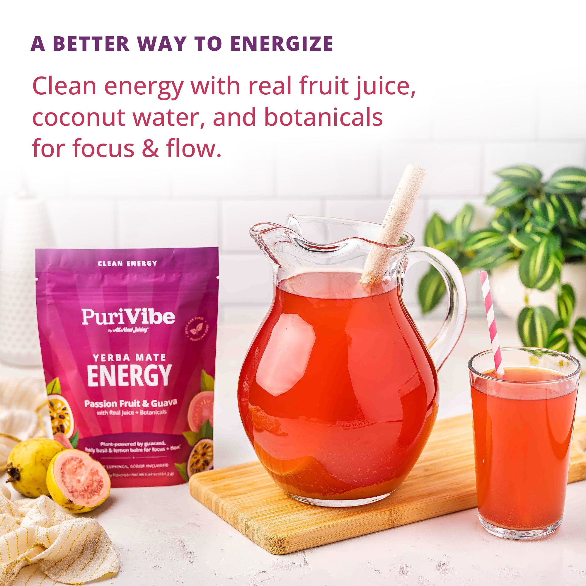 PuriVibe Clean Energy Yerba Mate Energy drink mix in a purple pouch, shown next to a glass pitcher filled with red juice and a glass of the same drink on a wooden board, with fruit pieces and a plant in the background.