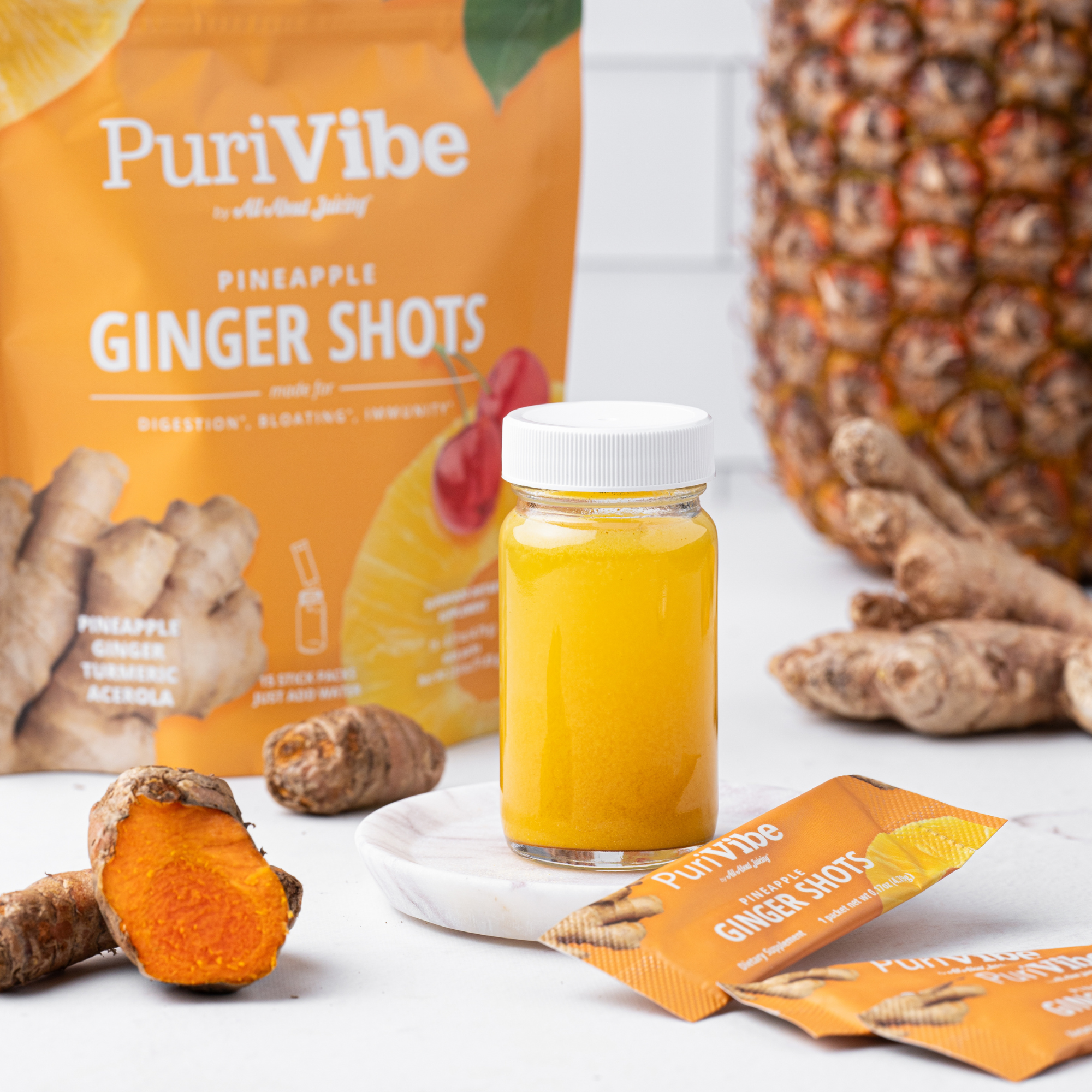 PuriVibe pineapple ginger shots with a bottle of juice, ginger root, and a pineapple on a white surface.