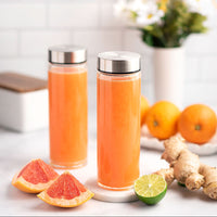 Two glass bottles with silver lids filled with orange juice, surrounded by citrus fruits and ginger on a light background.